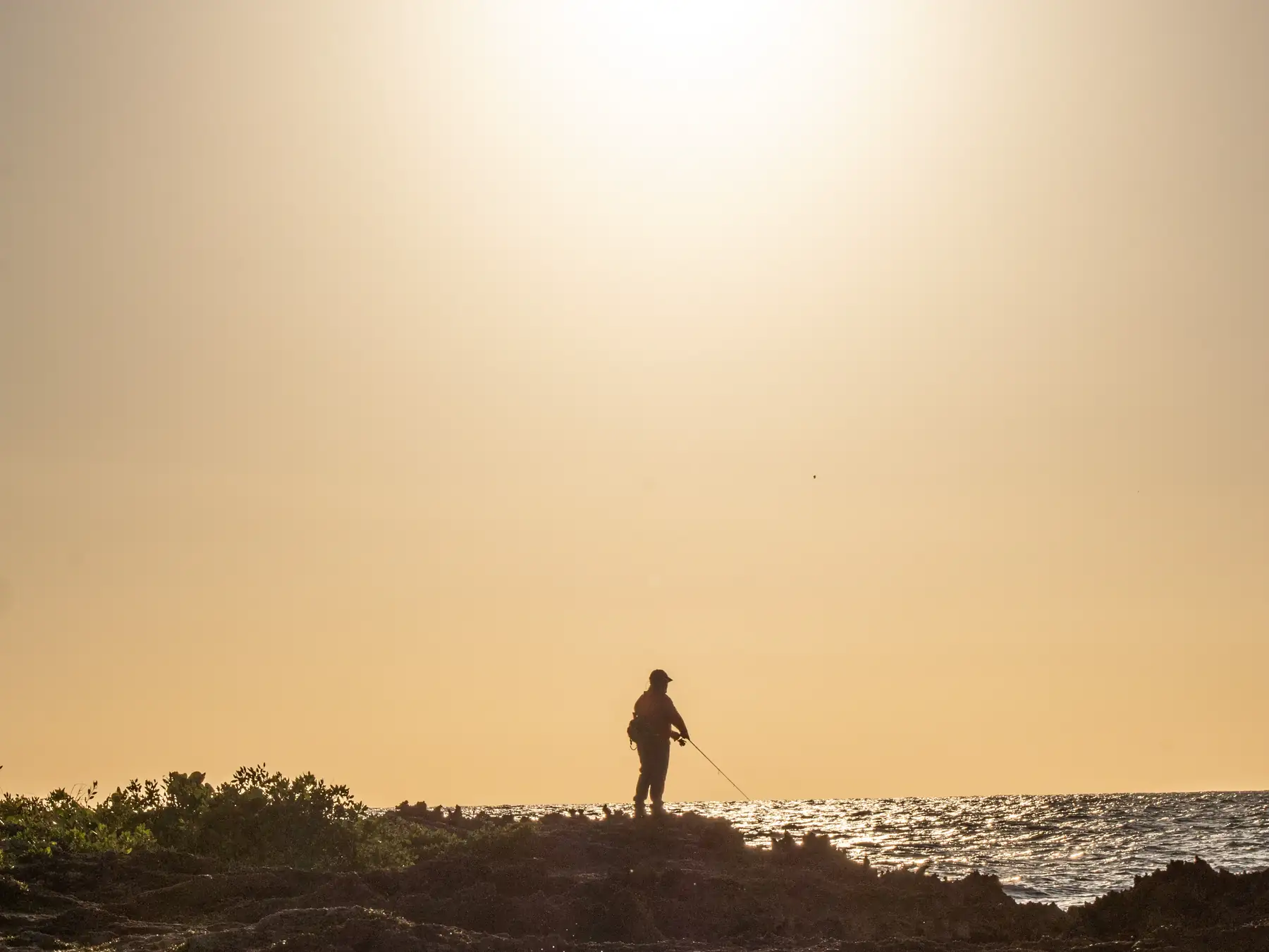 Fisherman on the rocky La Romana coast at sunset