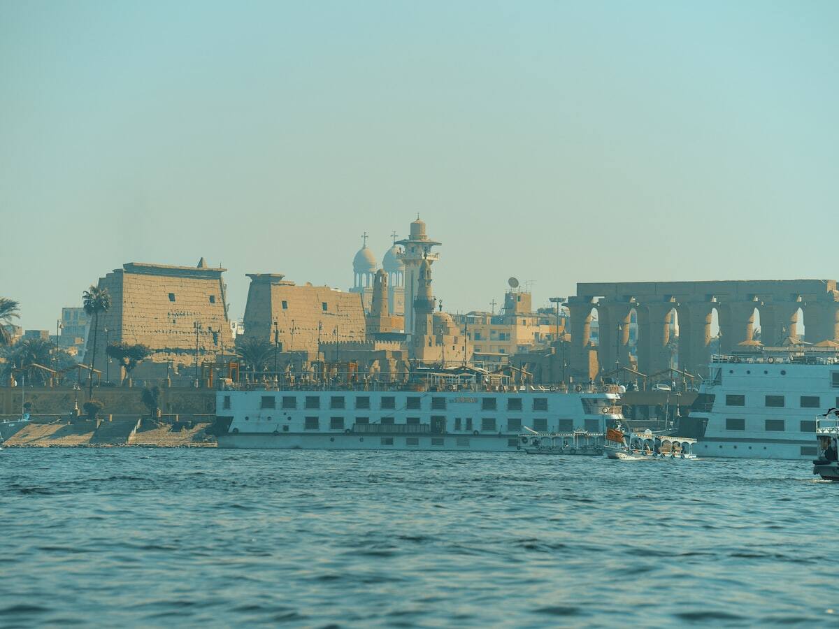 Nile cruise boats docked below ancient temple ruins in Luxor, Egypt