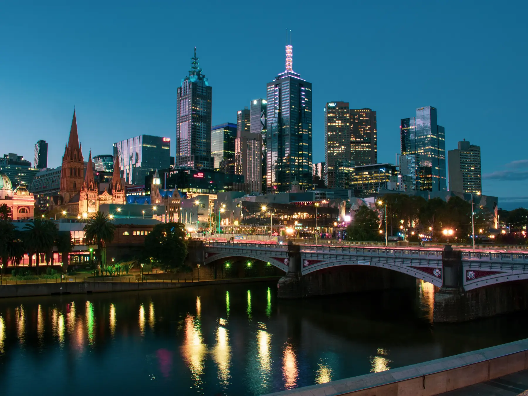 Princes Bridge and central Melbourne illuminated beside the Yarra River at twilight.
