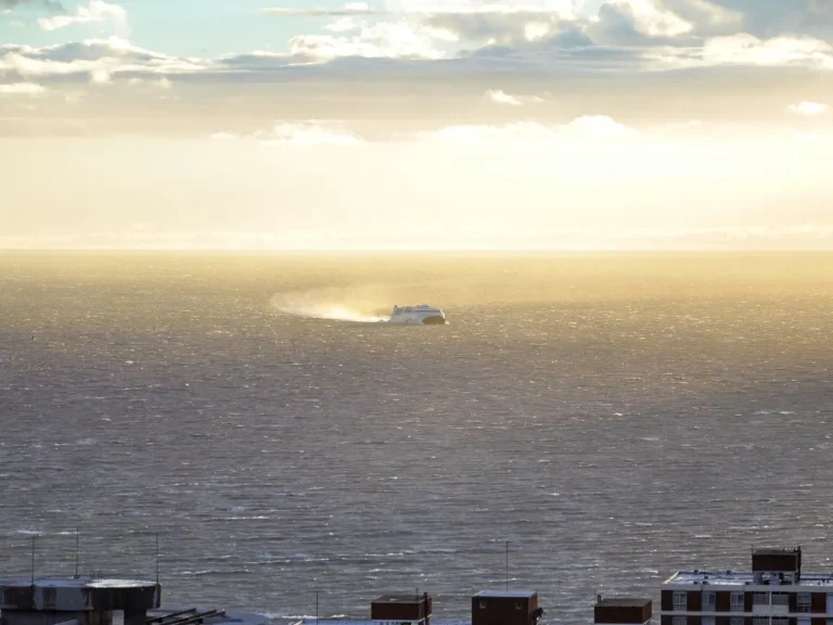 A passenger ferry crossing Montevideo harbor beneath sunlit clouds.
