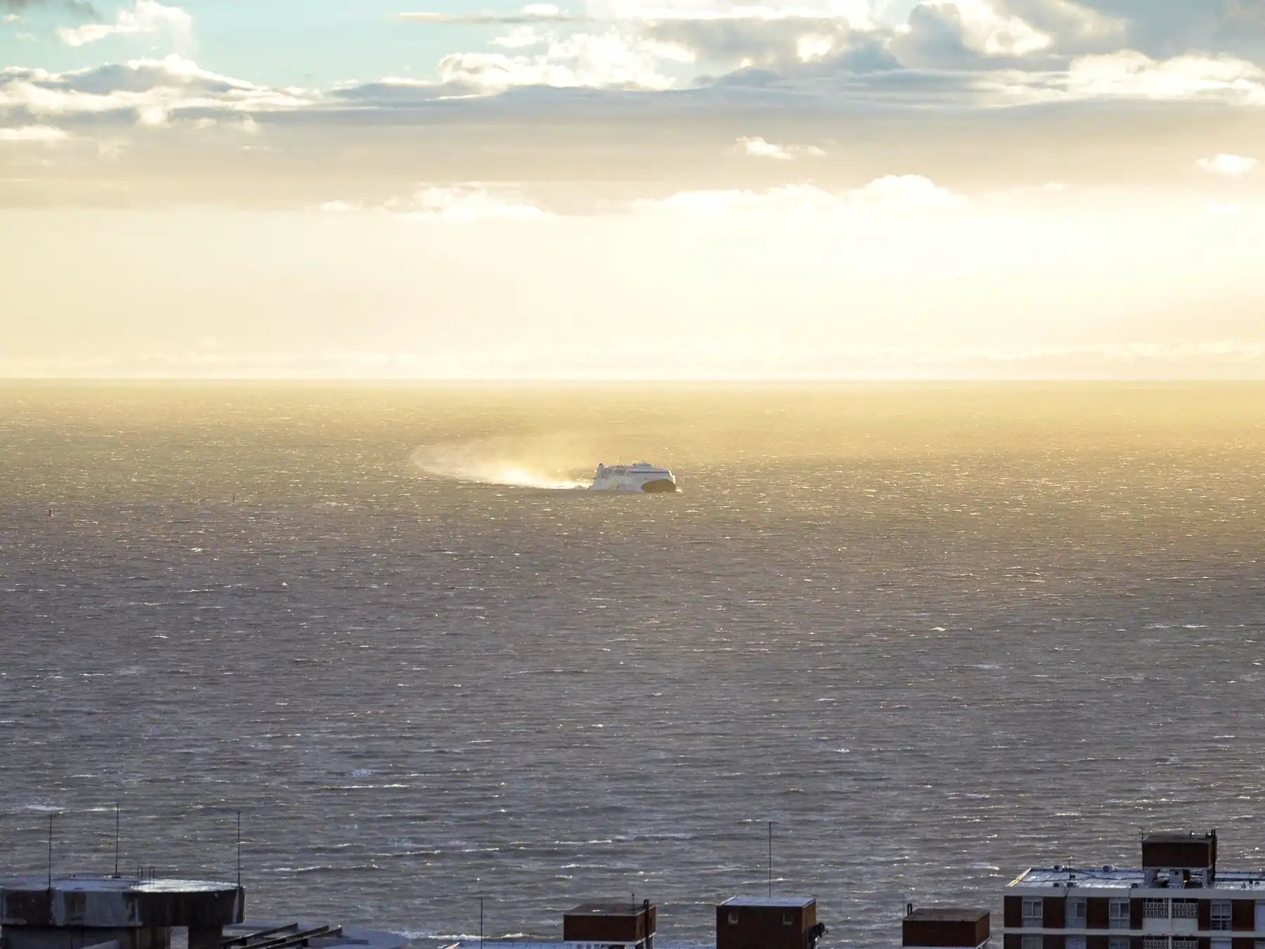 A passenger ferry crossing Montevideo harbor beneath sunlit clouds.
