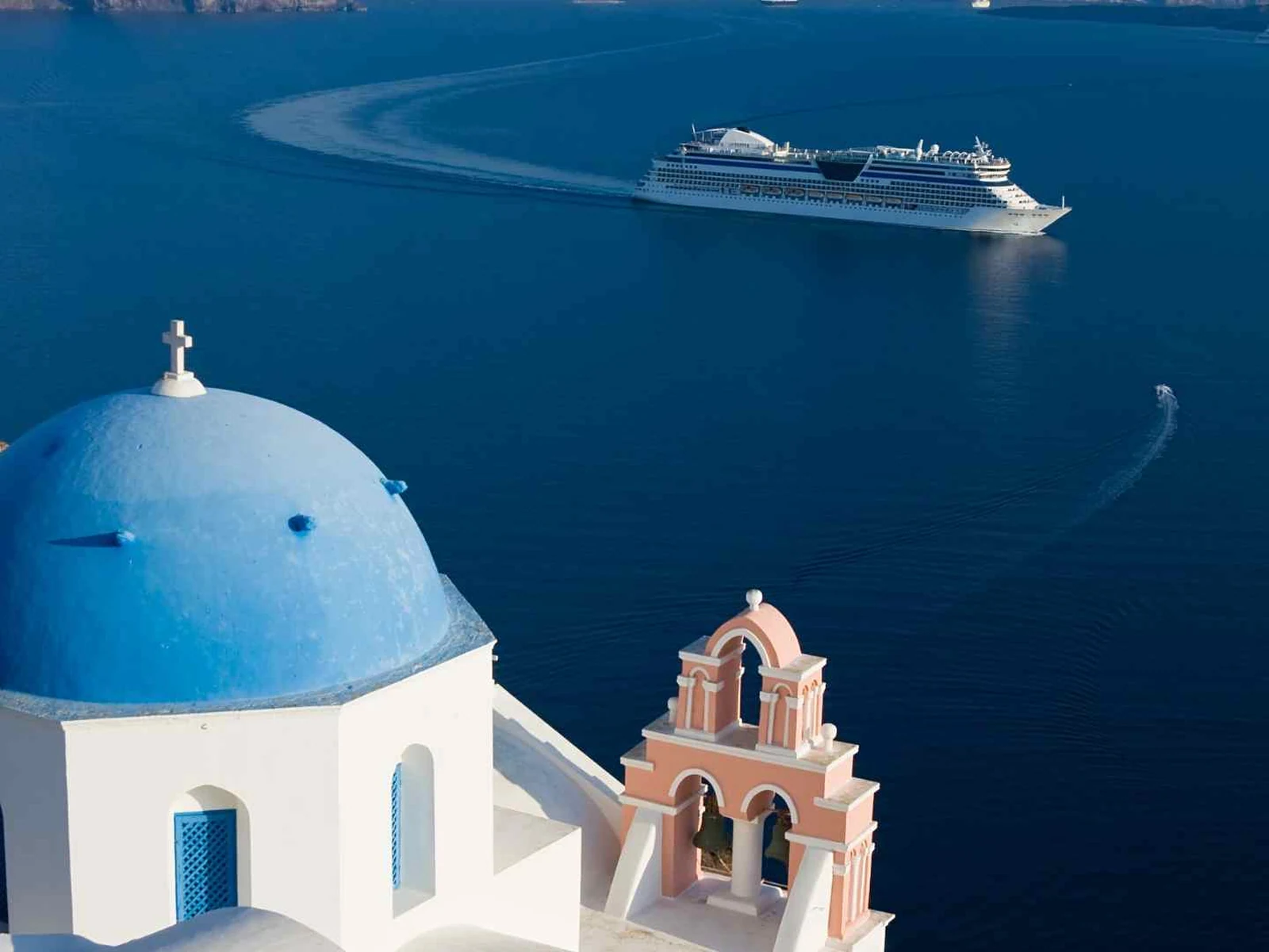Blue-domed Santorini church overlooking a cruise ship in the caldera