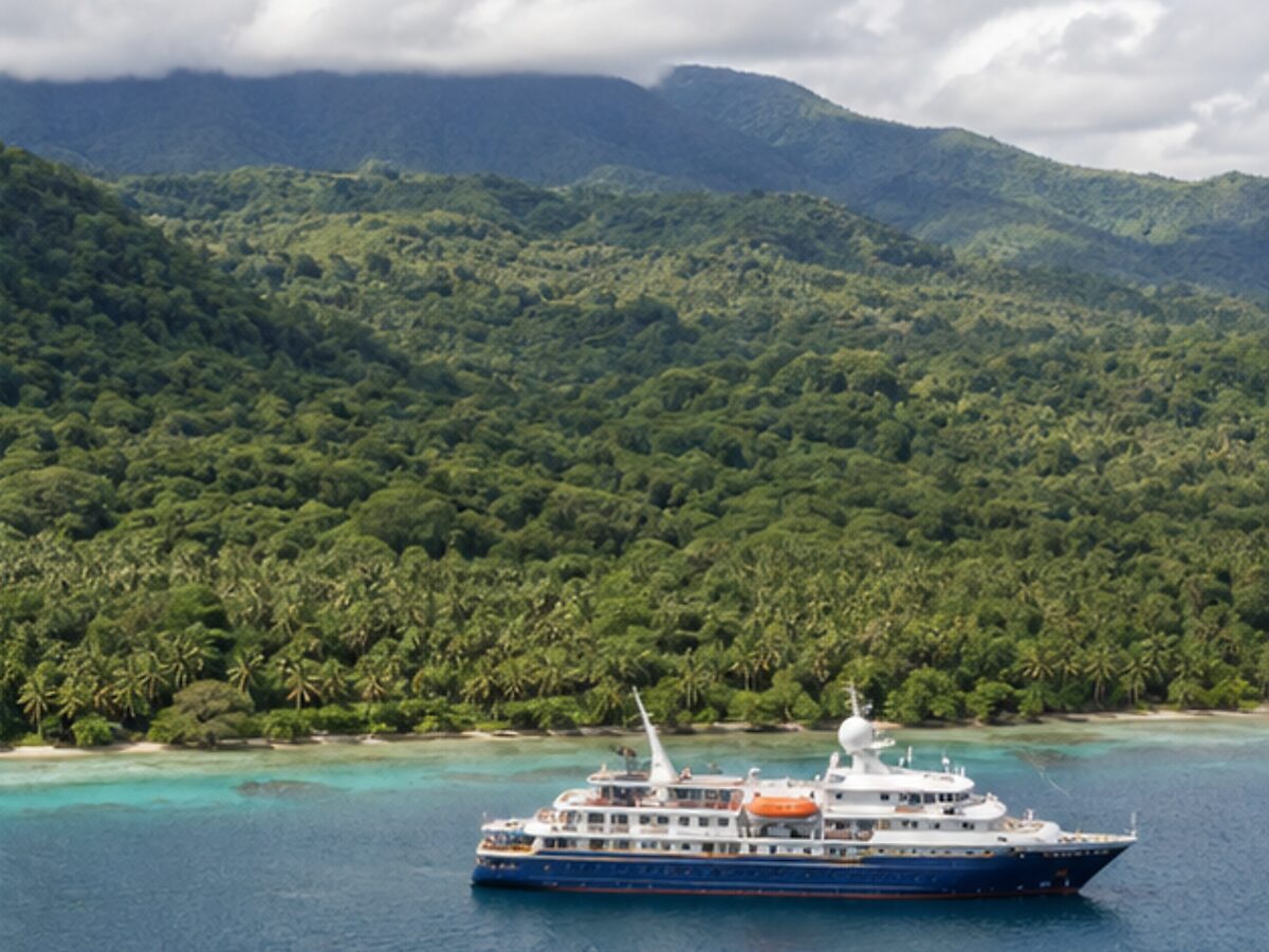 Expedition cruise ship off a lush tropical coastline in Papua New Guinea