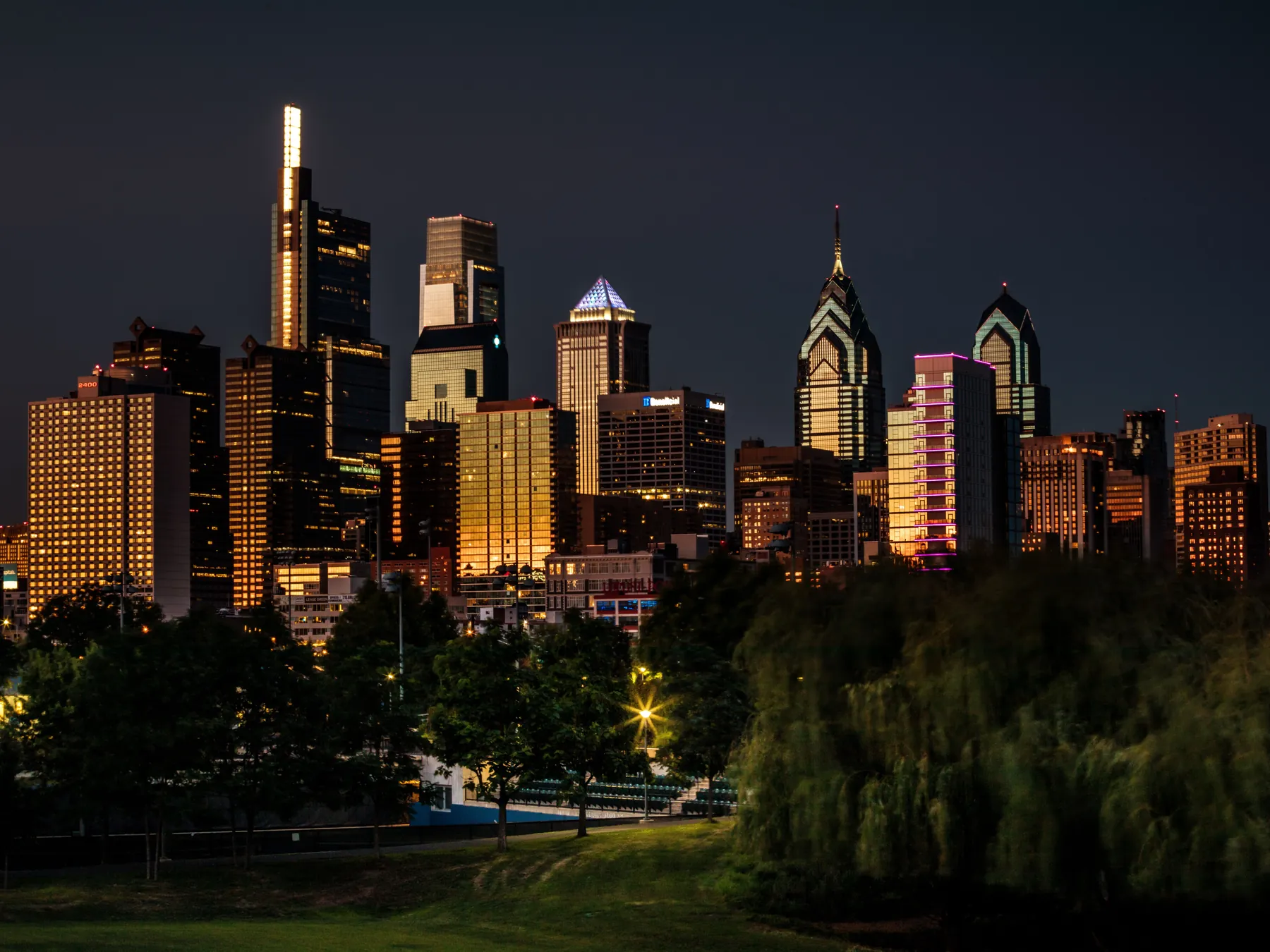 Philadelphia skyline viewed across green parkland at dusk