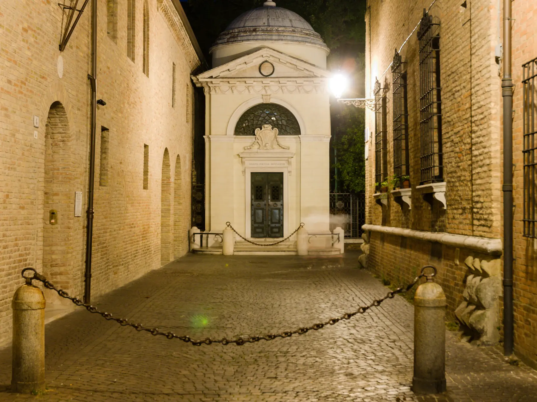 Dante Alighieri's white marble tomb illuminated at night in Ravenna, Italy.