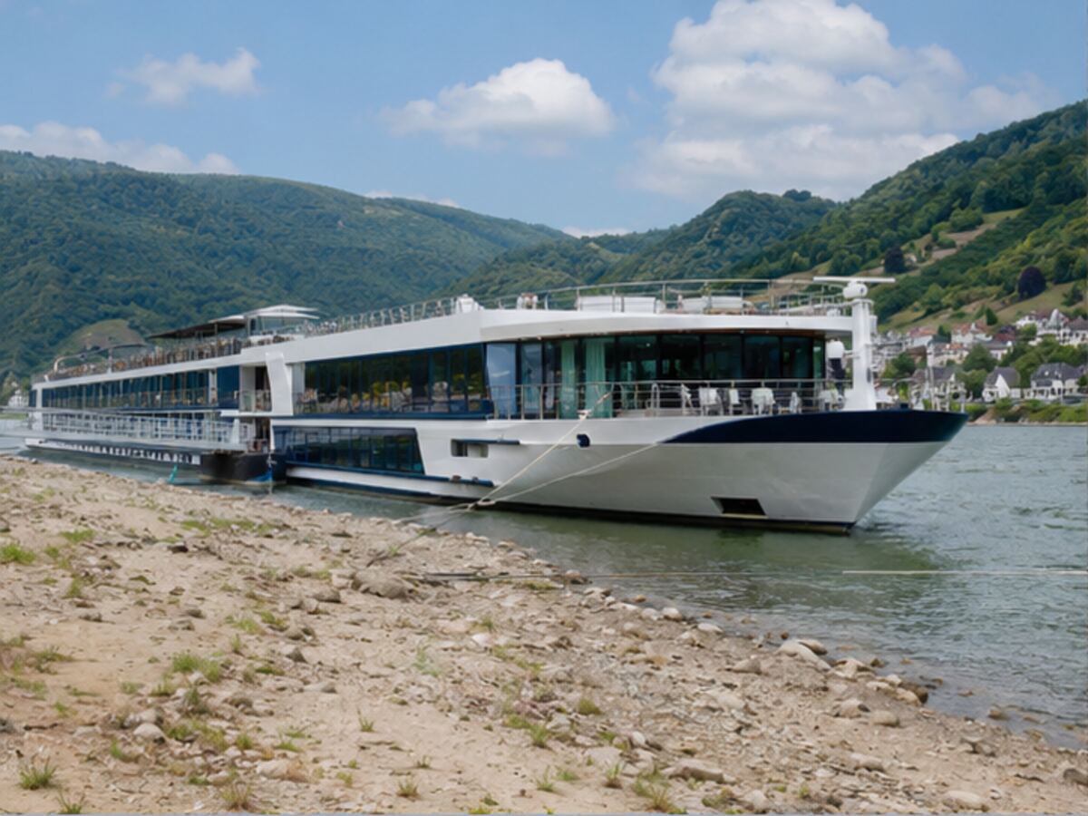 A river cruise ship sailing beside an exposed rocky riverbank during low water
