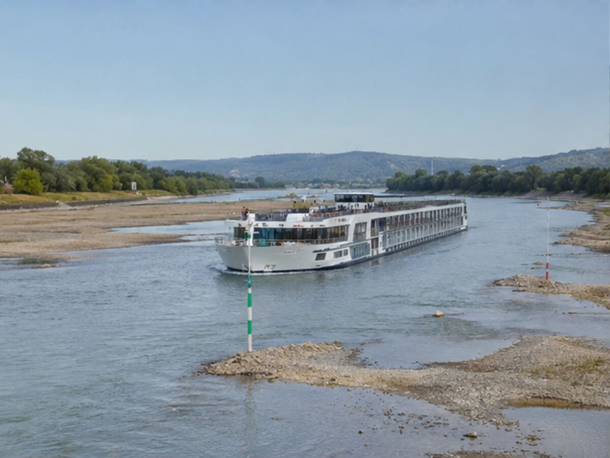 A river cruise ship navigating a narrow channel surrounded by exposed riverbed