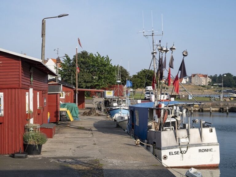 Fishing boats moored beside red harbor buildings in Rønne, Bornholm