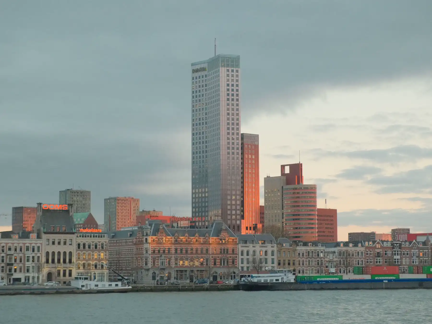 Modern and historic buildings along Rotterdam's riverfront in soft evening light.