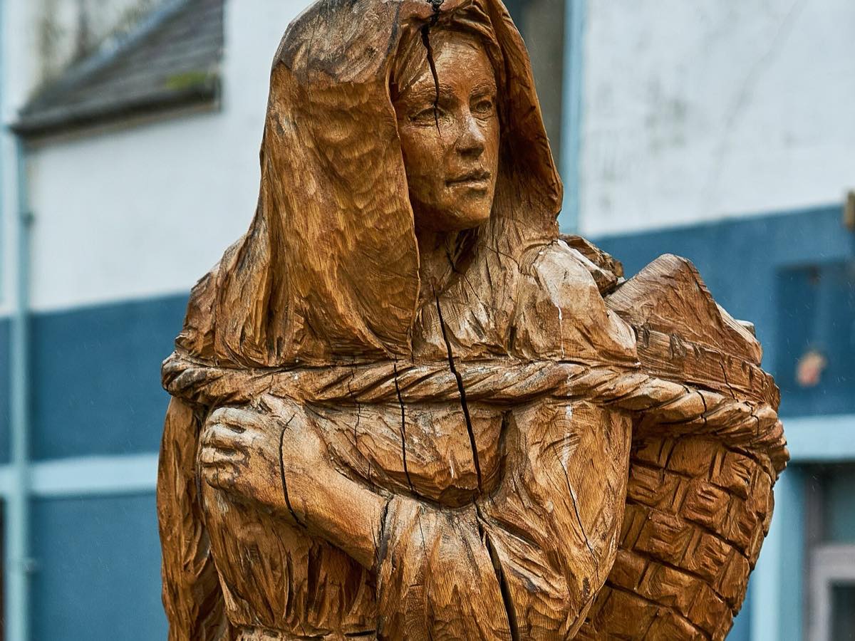 Wooden Peat Lady sculpture in Stornoway depicting a woman carrying a peat basket