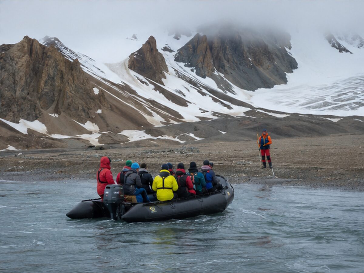 Expedition group approaching a remote Svalbard shore by Zodiac with a guide waiting