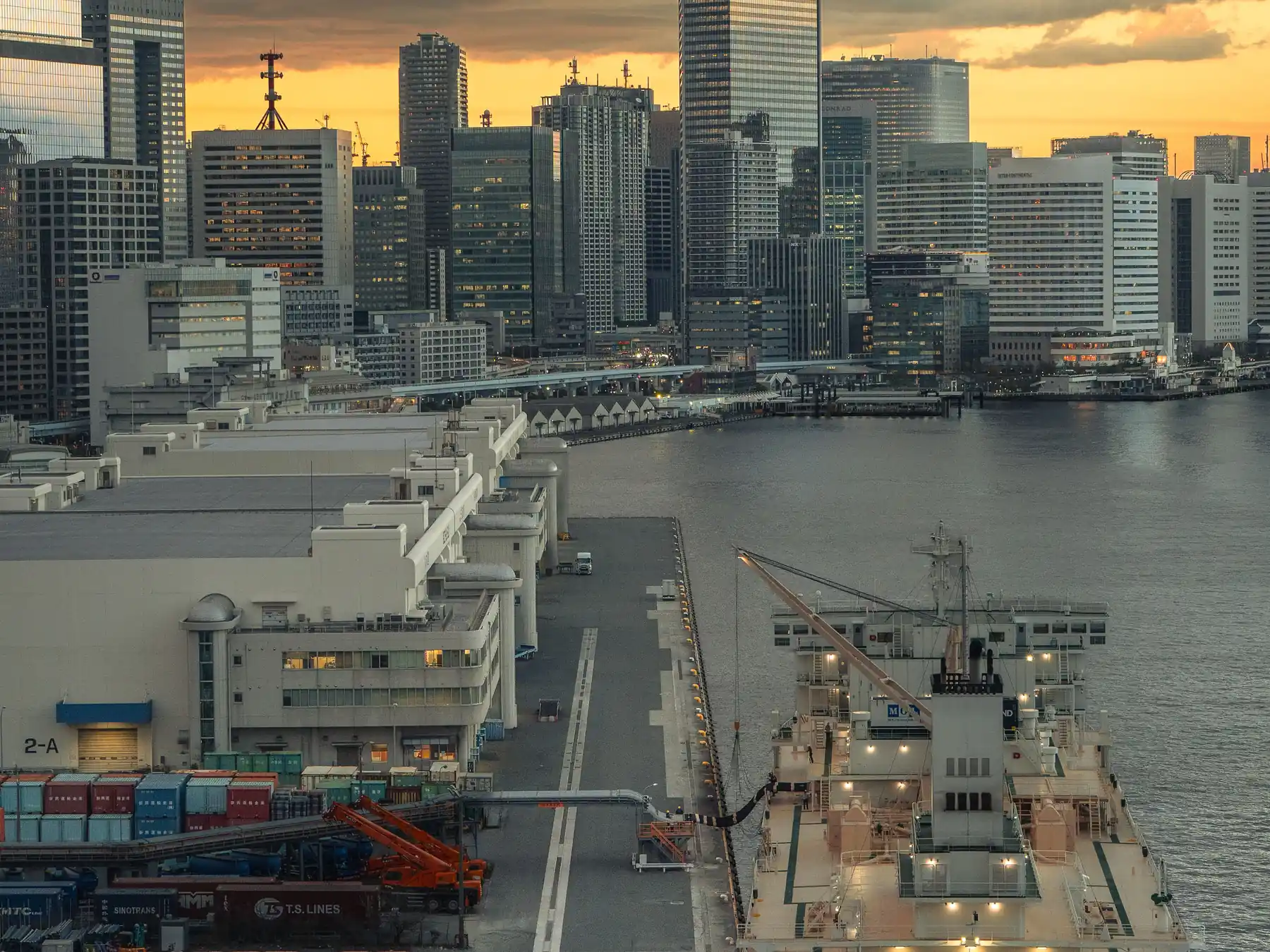 Tokyo's harbor, ships, and skyline beneath a dramatic sunset sky.