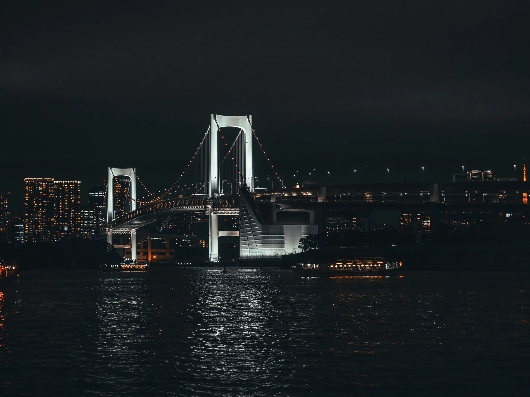 Rainbow Bridge and the Tokyo skyline illuminated above the water at night.
