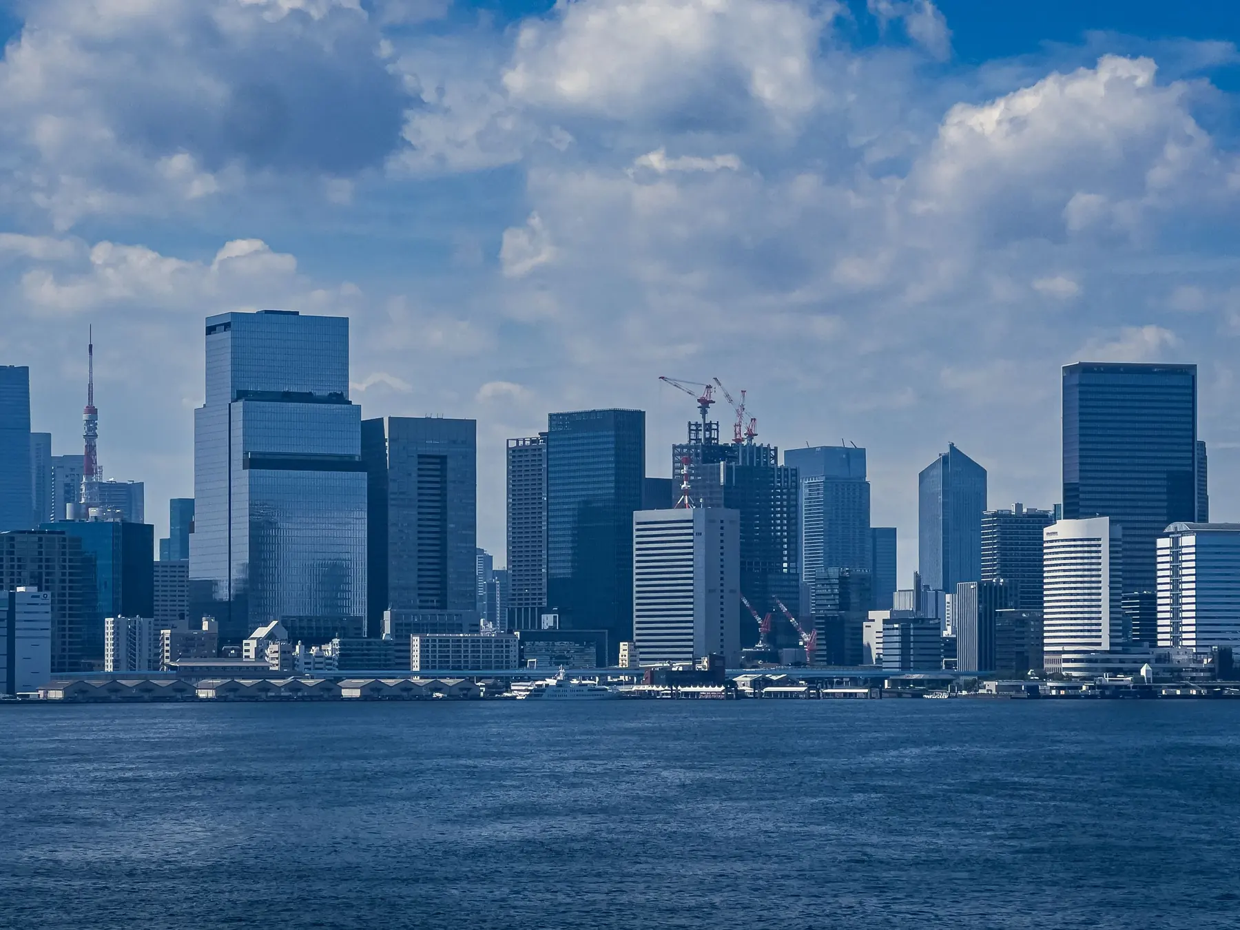 Modern skyscrapers lining Tokyo's waterfront under a bright blue sky.
