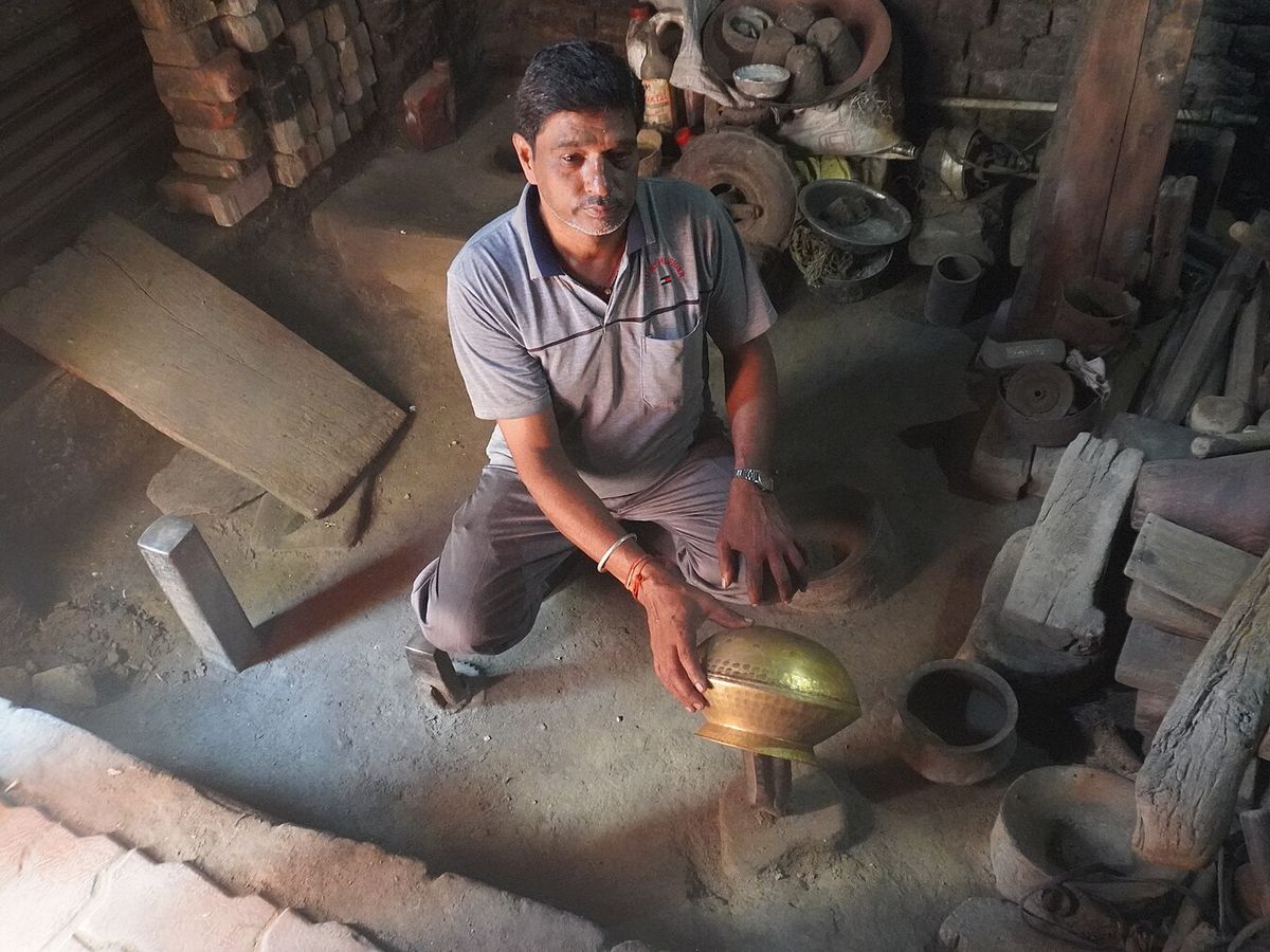 Indian brass artisan shaping a hammered metal utensil in a traditional workshop