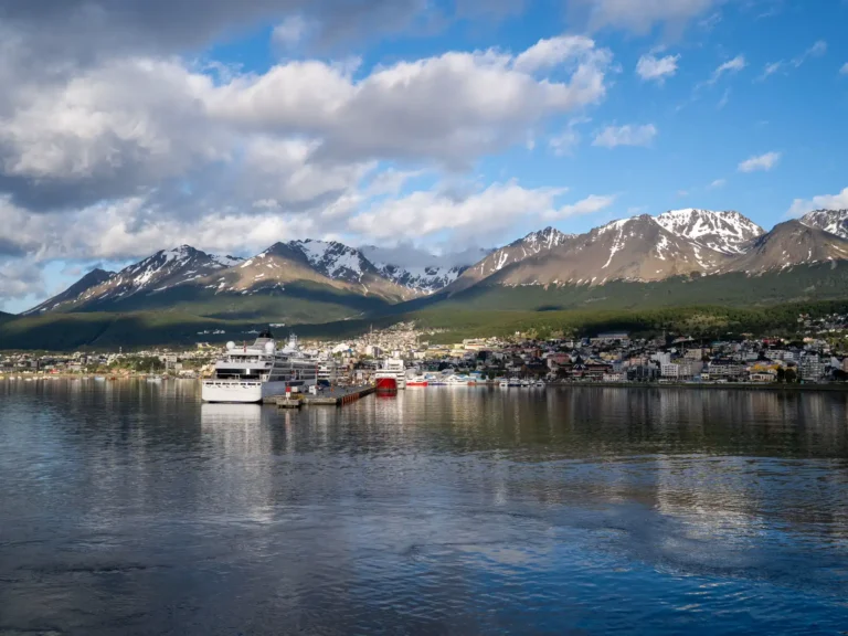 Ships and waterfront buildings in Ushuaia harbor beneath the Andes mountains.