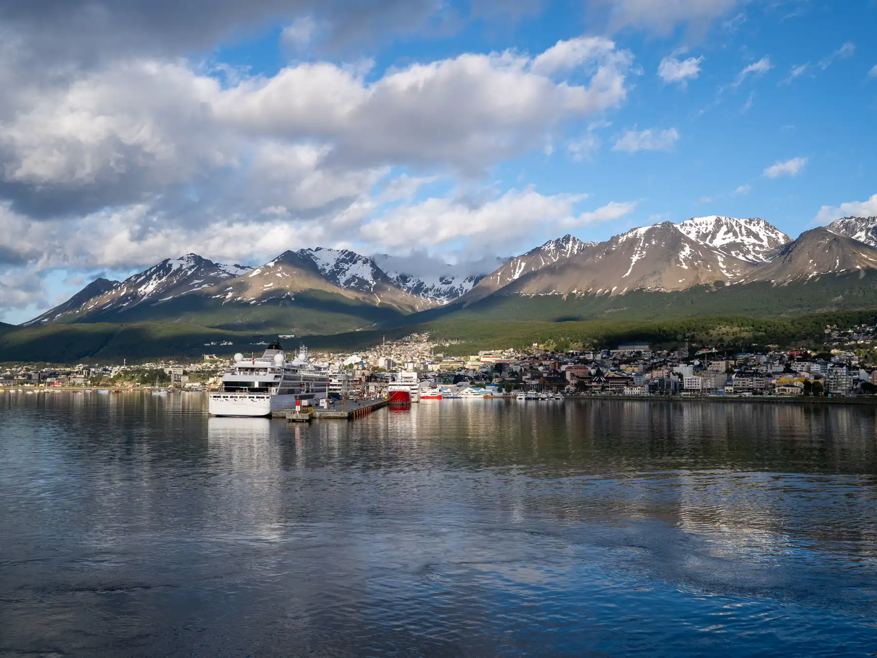 Ships and waterfront buildings in Ushuaia harbor beneath the Andes mountains.
