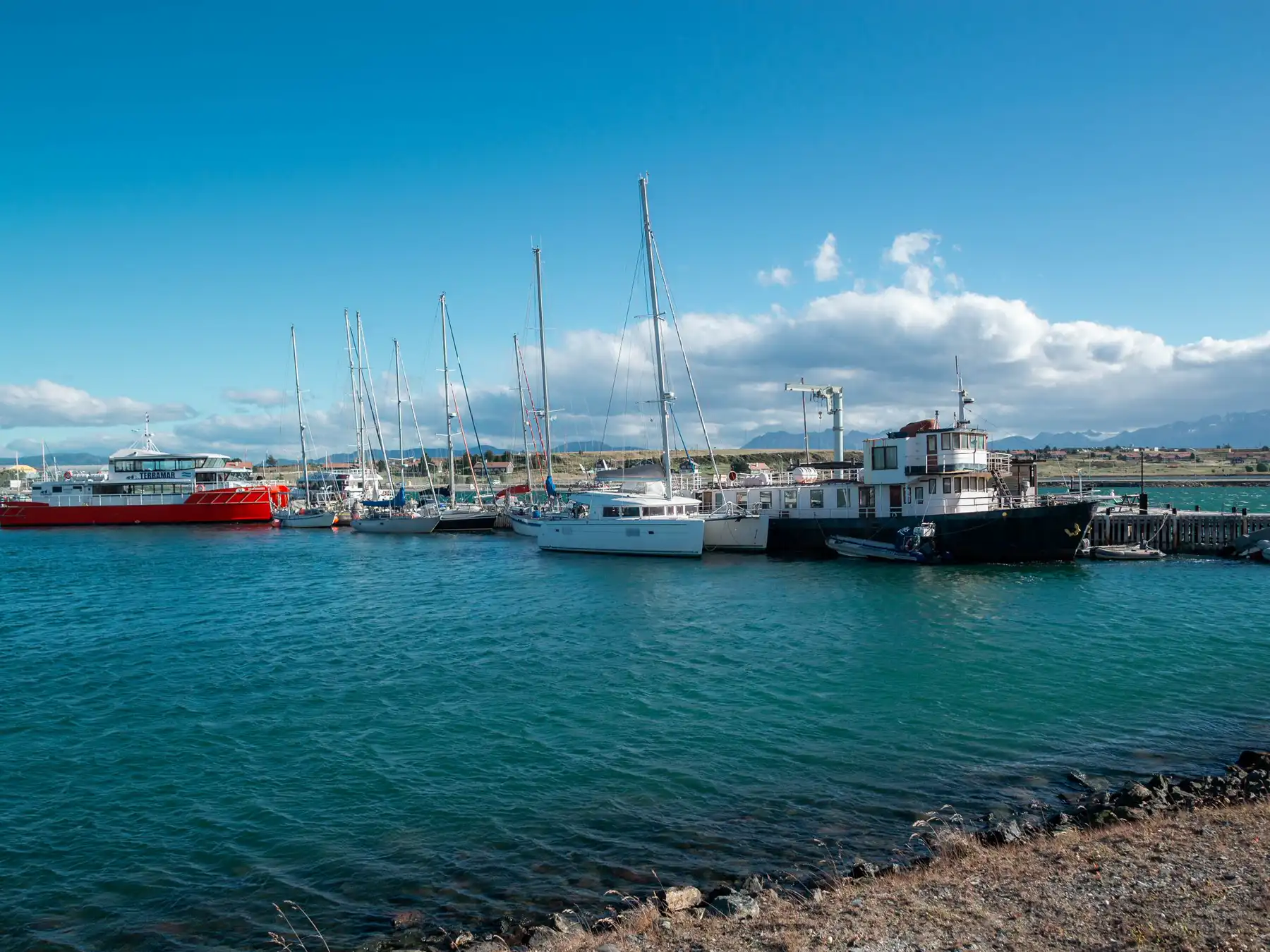 Sailboats and passenger vessels moored in the blue waters of Ushuaia marina.