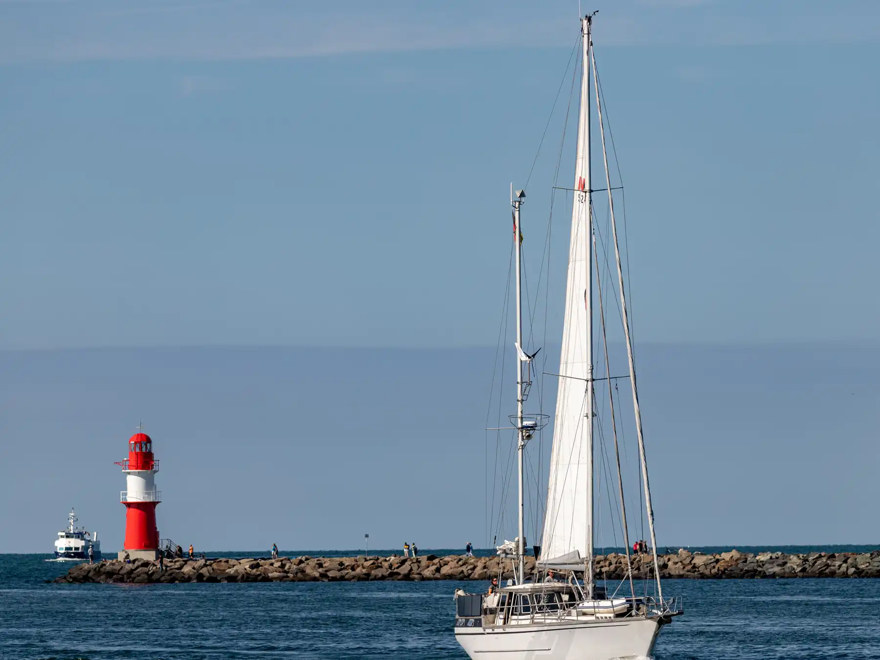 A sailboat passing the red breakwater lighthouse at Warnemünde harbor.