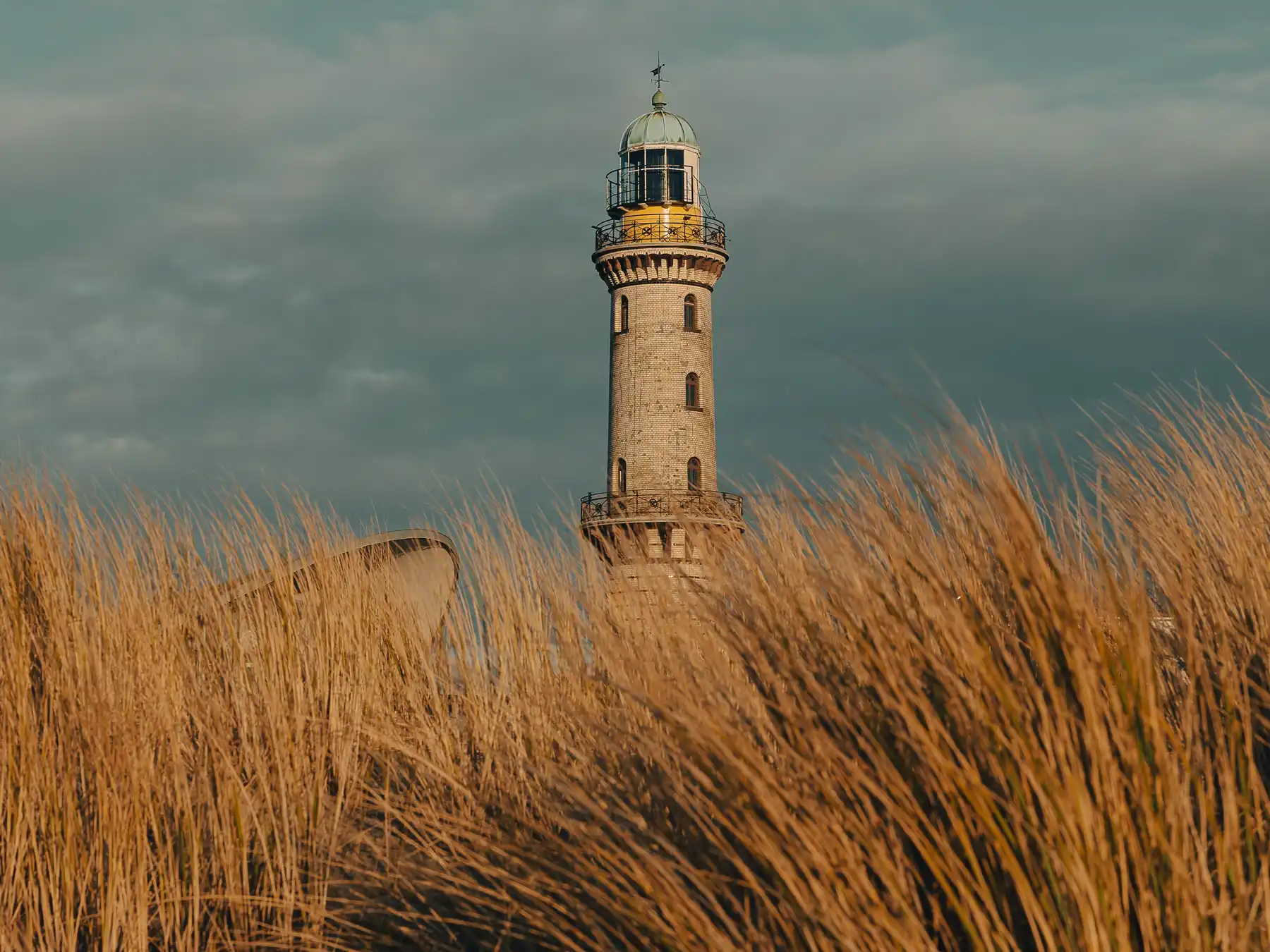 Warnemünde Lighthouse rising above coastal dune grass under a dramatic sky.