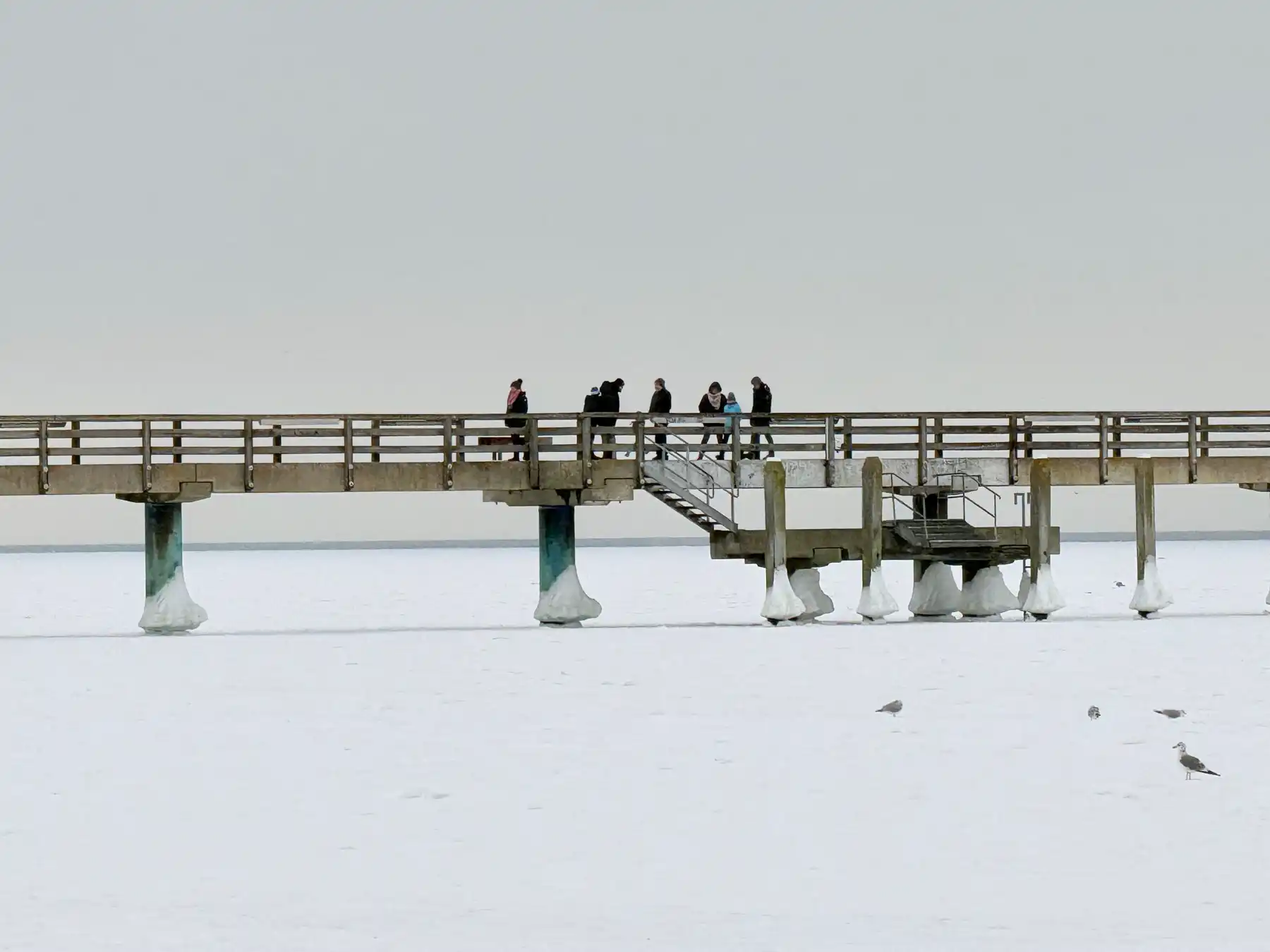 Visitors walking on a snow-covered pier above frozen water in Warnemünde.