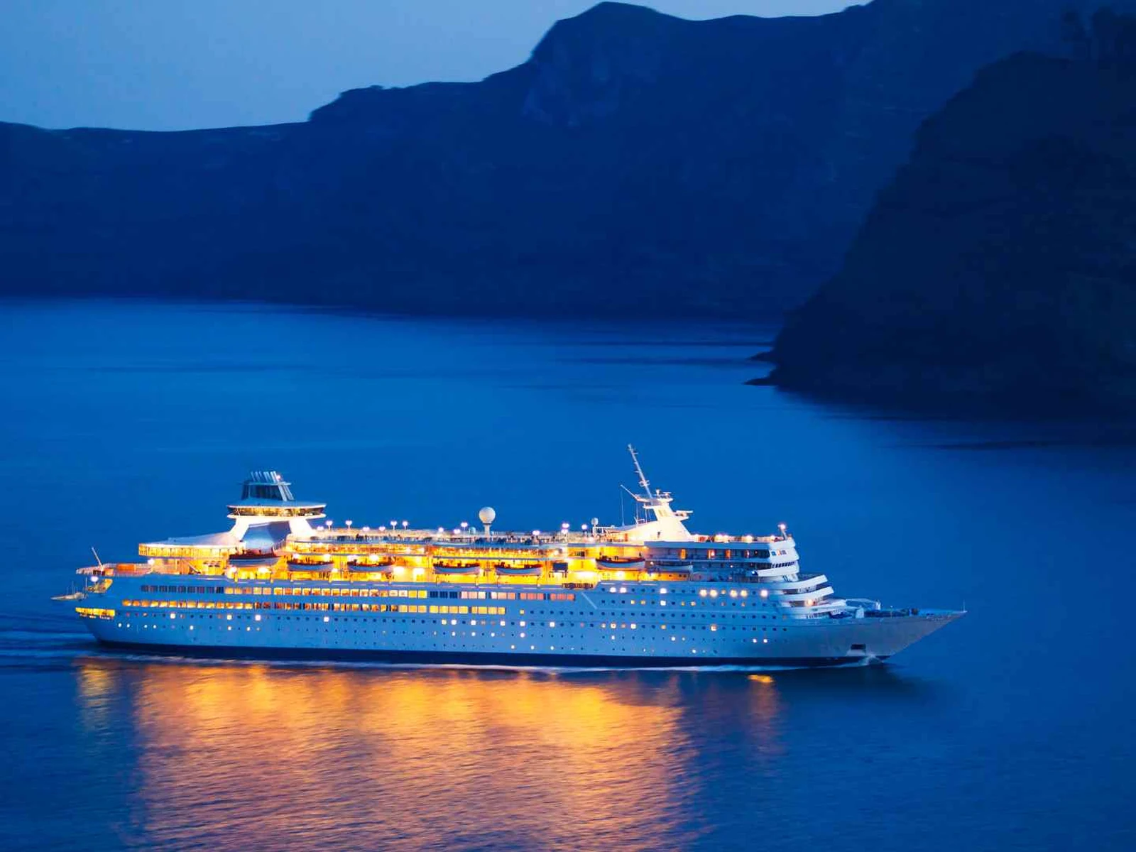 Cruise ship sailing through a mountainous Mediterranean bay at dusk
