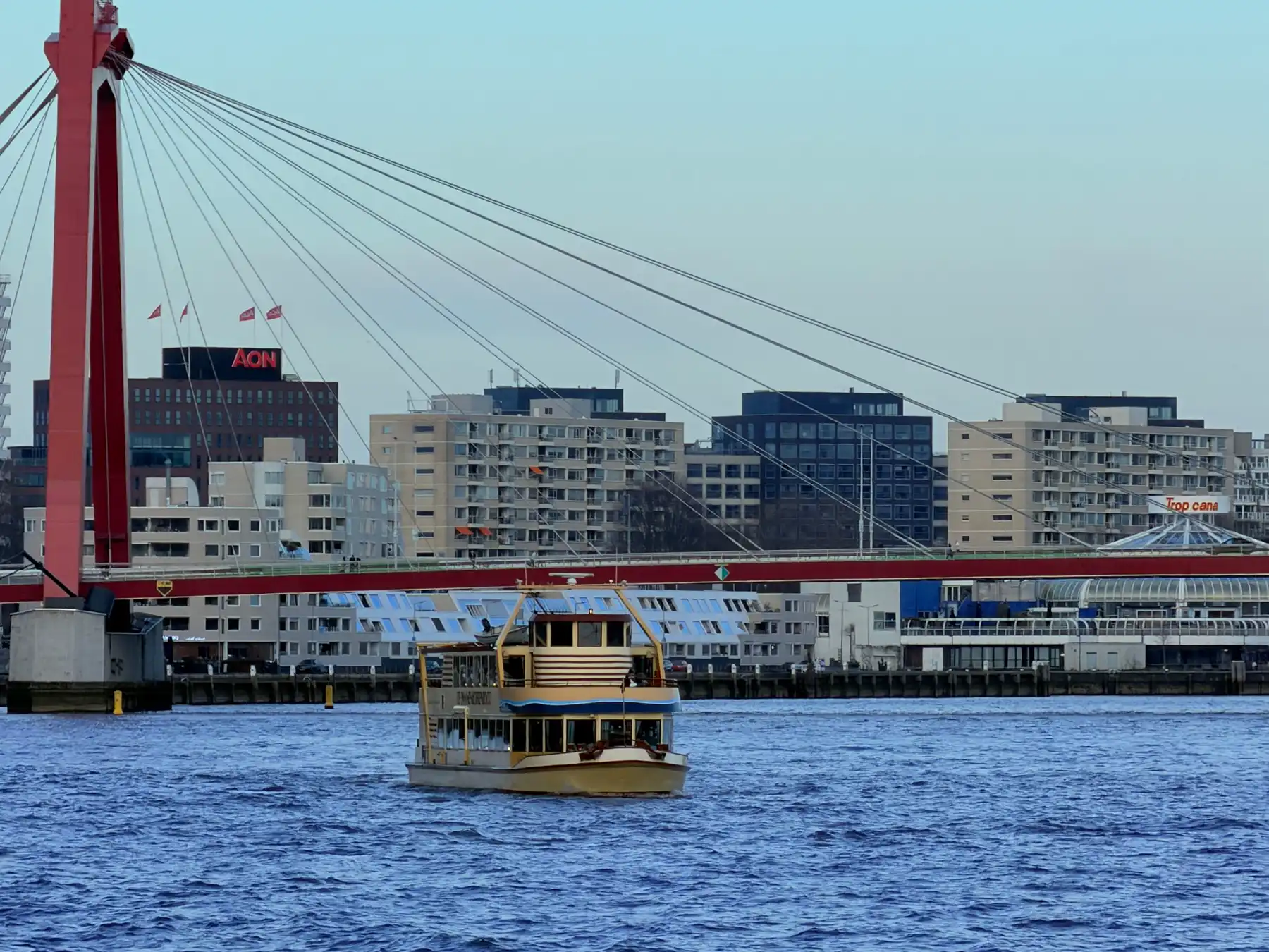A passenger boat crossing the Nieuwe Maas beside Rotterdam's red Willemsbrug.