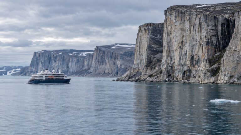 Expedition cruise ship offshore beside Akpatok Island’s limestone cliffs