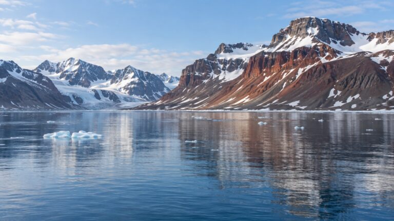 Quiet Ayerfjorden anchorage beneath snow-patched red mountains