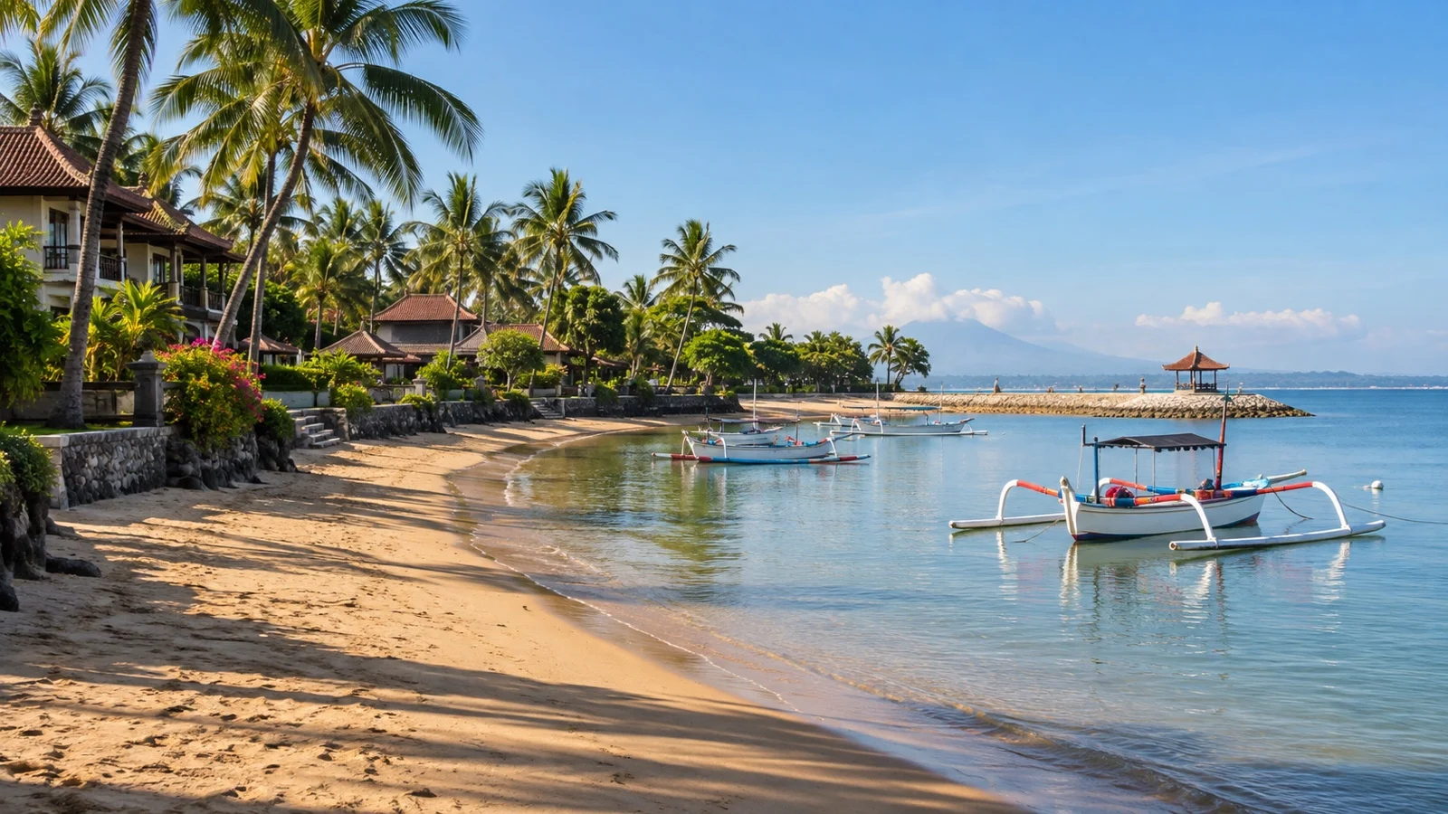 Sanur beachfront in Bali with low resort hotels, palms and traditional outrigger boats on calm water