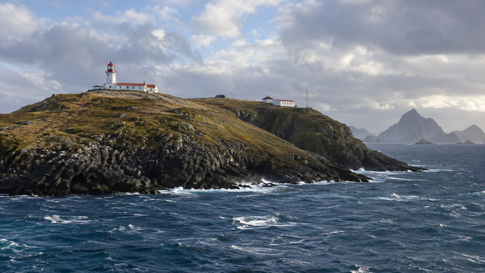 Cape Horn remote lighthouse and naval station buildings on treeless grassy island ridge beneath clouds, no people