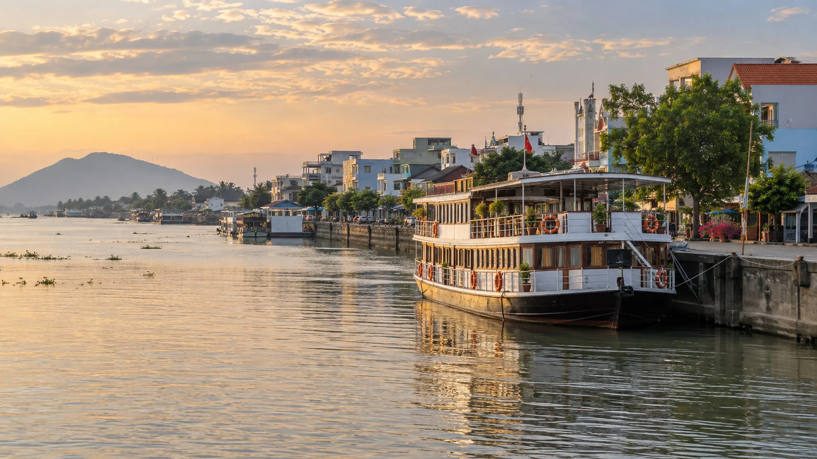 Small river cruise vessel moored at Chau Doc Vietnam on a broad Mekong Delta waterway, riverside town behind
