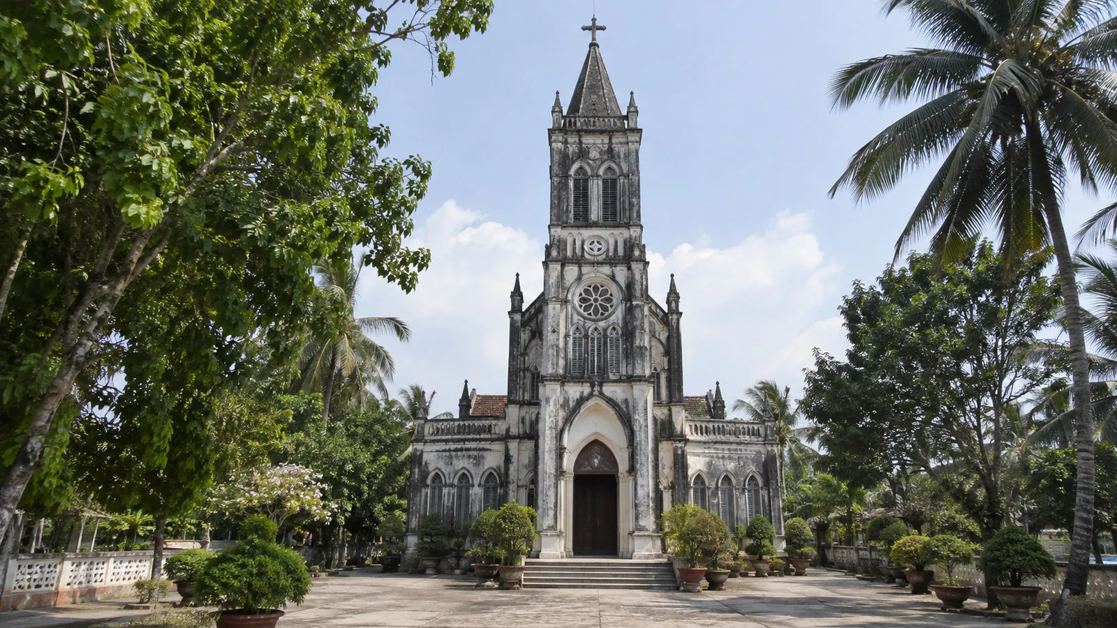 Cu Lao Gieng Church facade on Mekong island Vietnam, old French colonial Gothic church amid tropical trees, no people