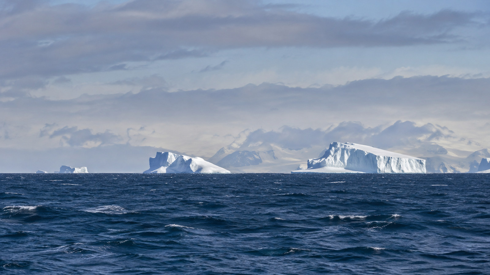 First distant Antarctic icebergs on the horizon after crossing the Drake Passage, cold blue water