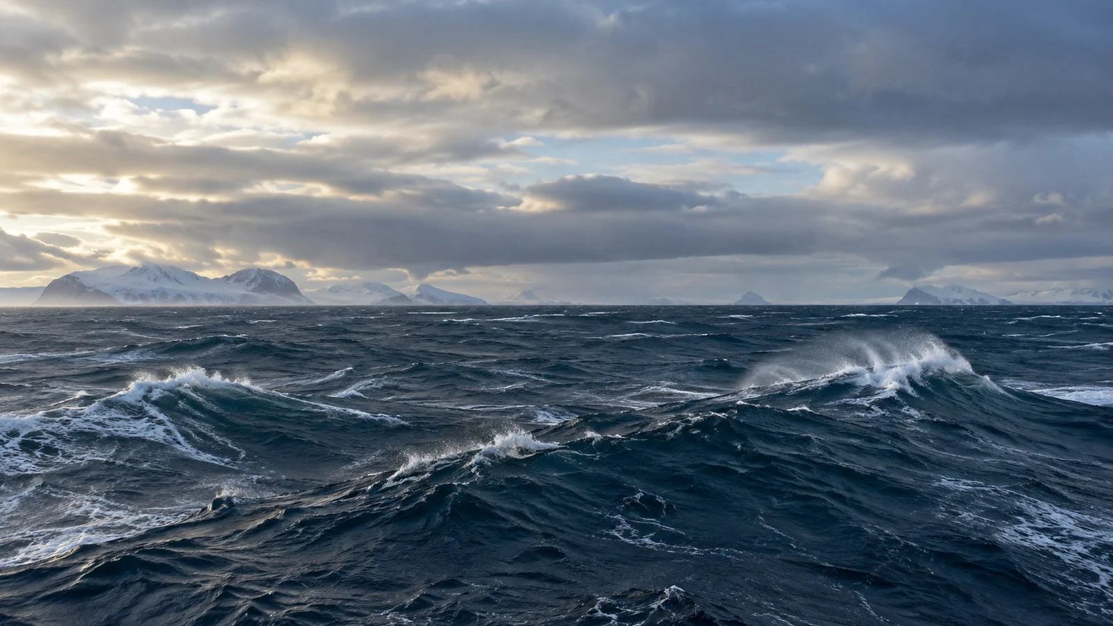 Rolling Southern Ocean waves and spray beneath layered clouds, wide horizon