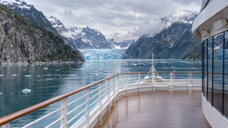 view from the empty deck of a large cruise ship sailing through Alaska's Endicott Arm fjord toward distant blue Dawes Glacier