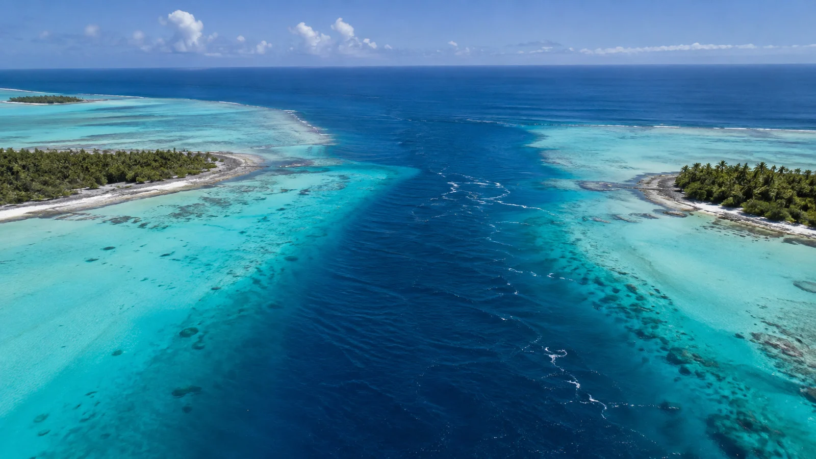 Aerial perspective of Garuae Pass Fakarava where deep blue ocean meets turquoise lagoon between low reef islands