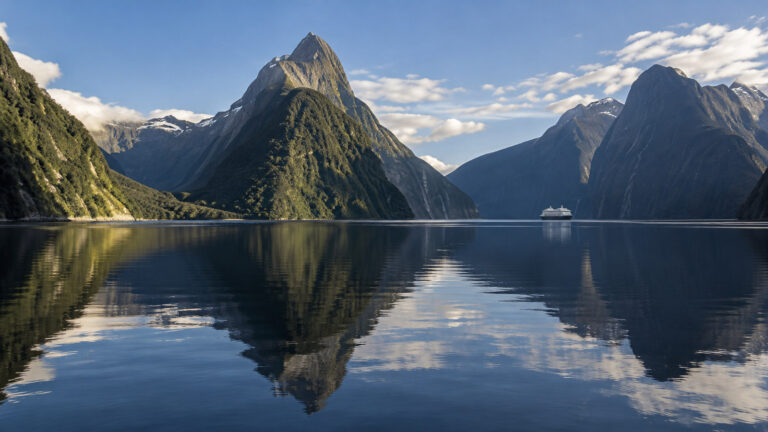 Milford Sound Piopiotahi New Zealand with iconic Mitre Peak reflected in dark fjord water and small cruise ship far away, no people