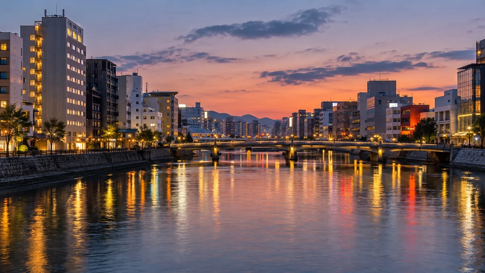 Nakasu riverfront in Fukuoka with bridges, compact hotels and city lights reflected in the water at dusk