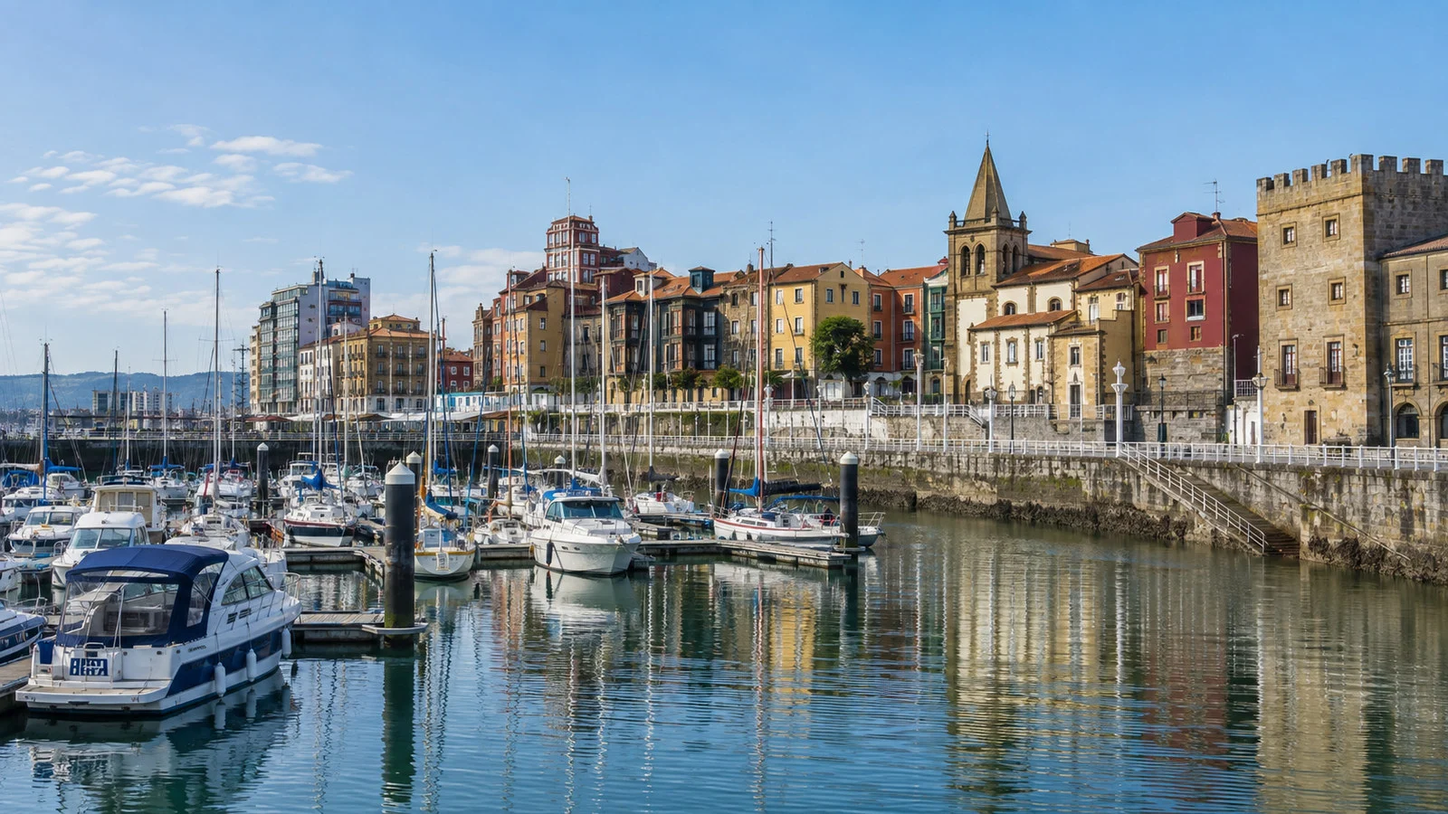 Gijon waterfront marina with colorful boats, promenade and old town buildings, no people