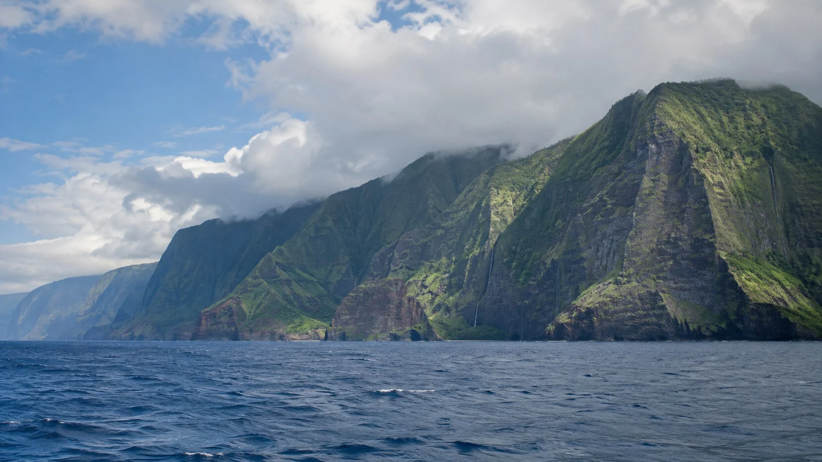 Molokai Hawaii towering sea cliffs seen from offshore Pacific water beneath clouds, no people