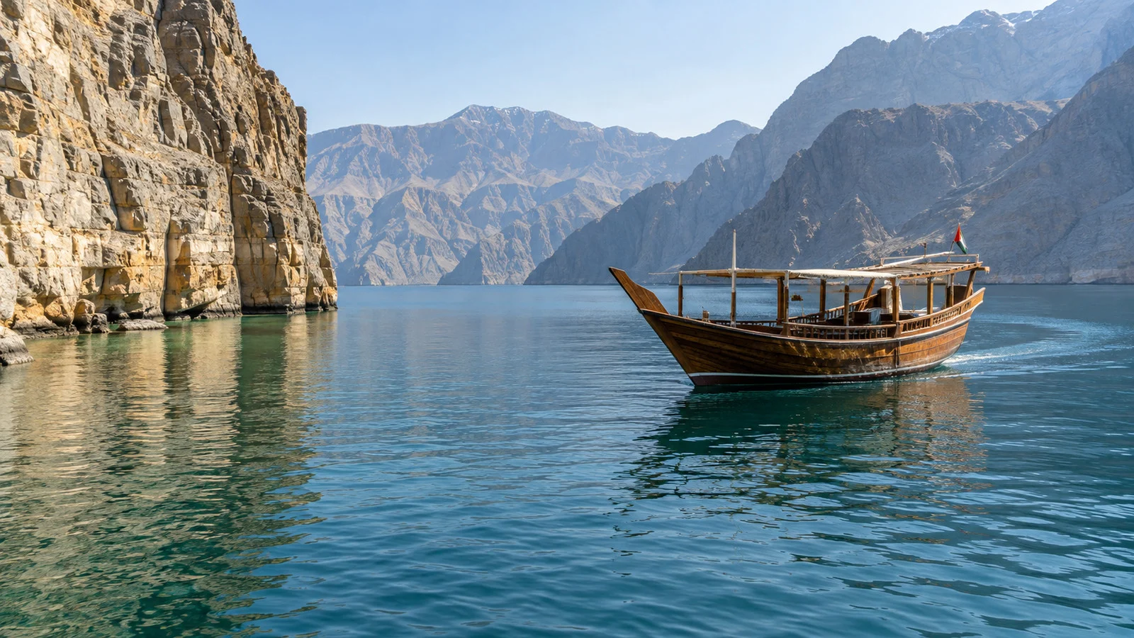 Traditional wooden dhow sailing among Musandam fjord cliffs