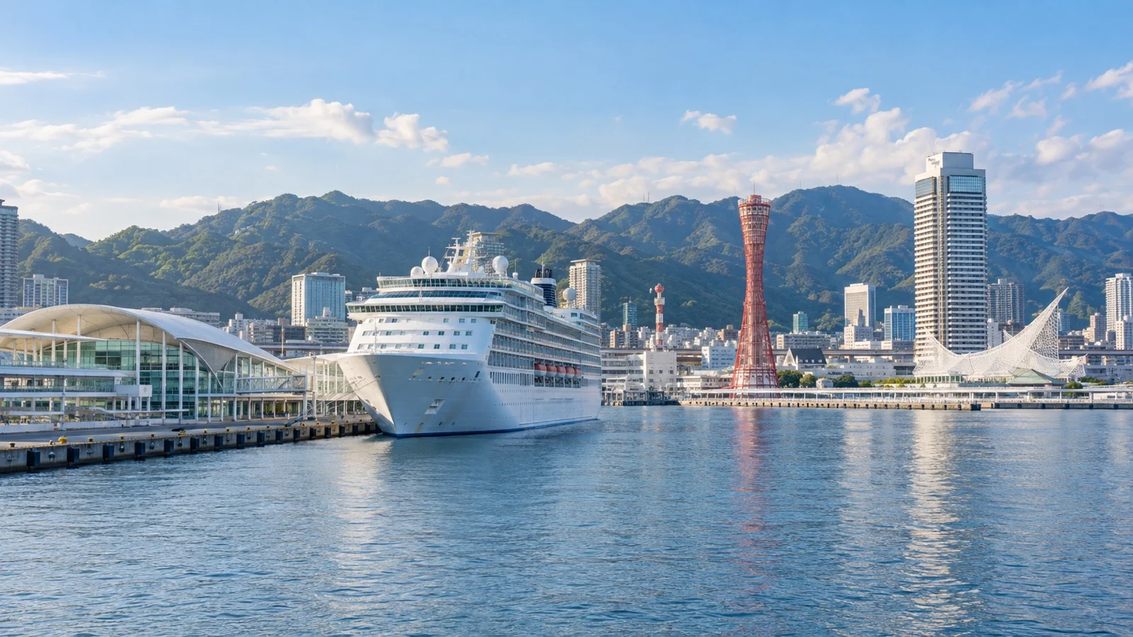 Kobe Port Terminal cruise berth with a white cruise ship beside Kobe Harbor and Mount Rokko behind the city