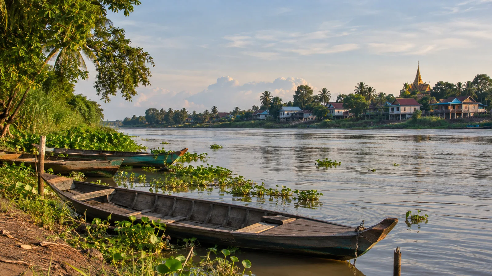 Mekong River bank near Koh Chen Cambodia with empty wooden boats, green vegetation and distant village, no people