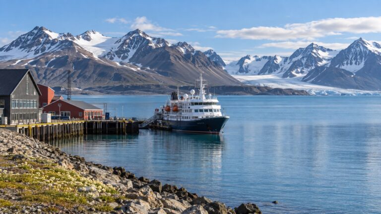 Longyearbyen cruise pier with a small Arctic expedition ship beside Isfjorden and rugged Svalbard mountains in summer daylight
