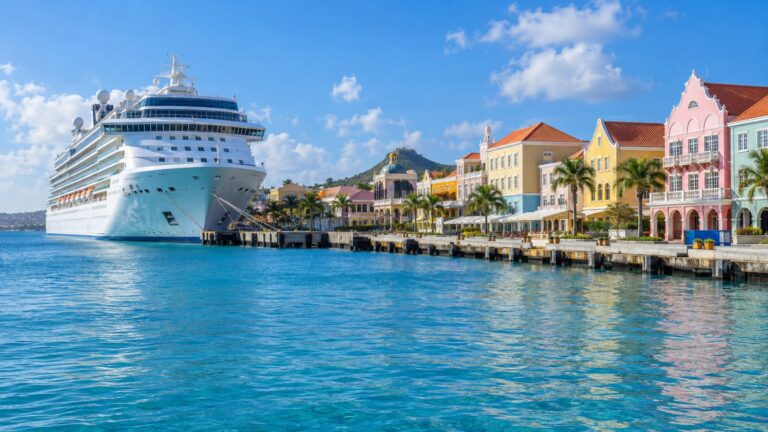 Oranjestad cruise terminal in Aruba with a large white cruise ship docked beside colorful Dutch Caribbean waterfront buildings