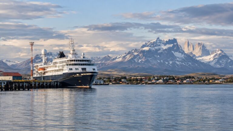 Small expedition cruise ship in Puerto Natales harbor with Patagonian mountains beyond