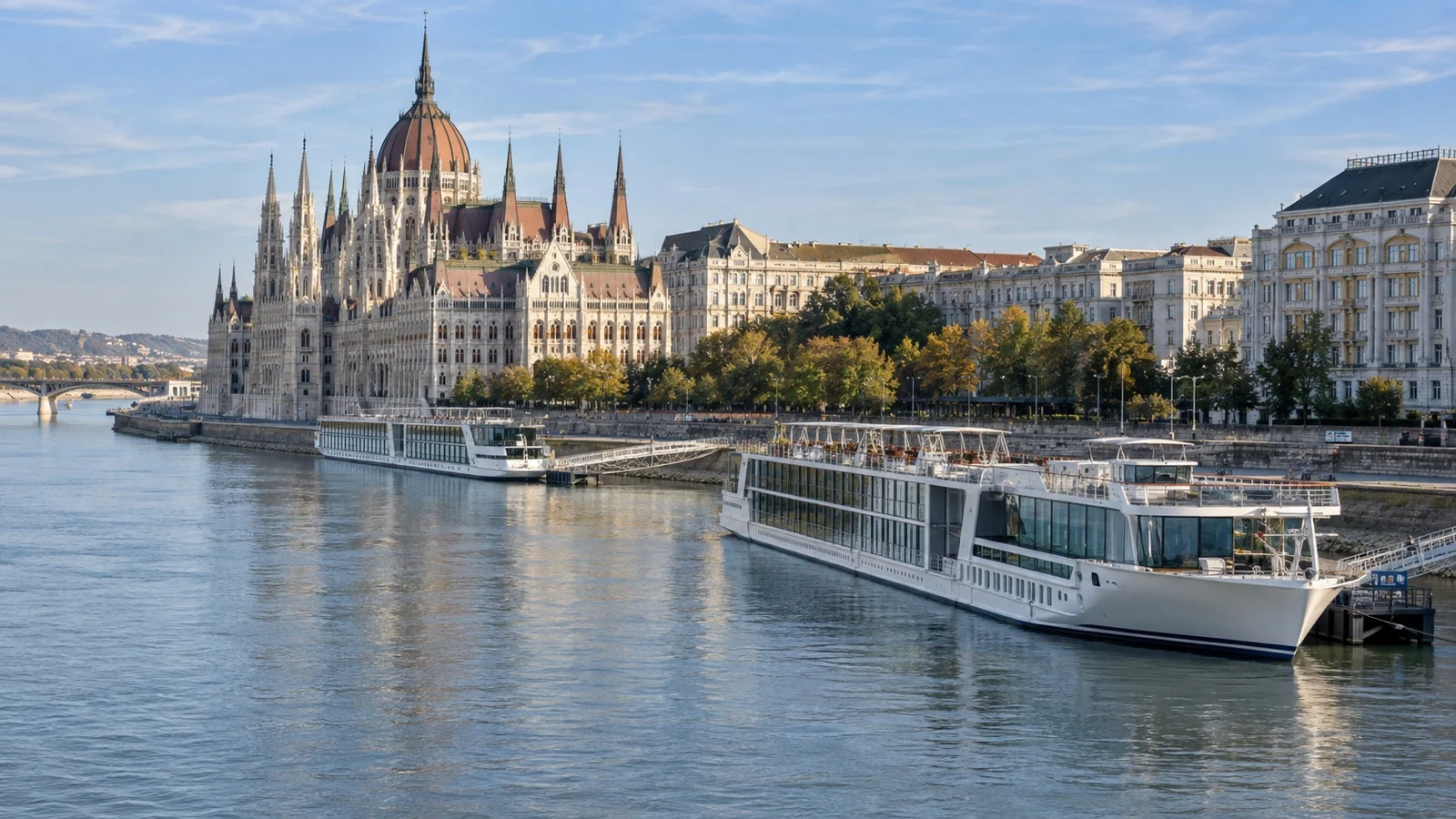 Two river cruise vessels at different moorings along a city riverfront