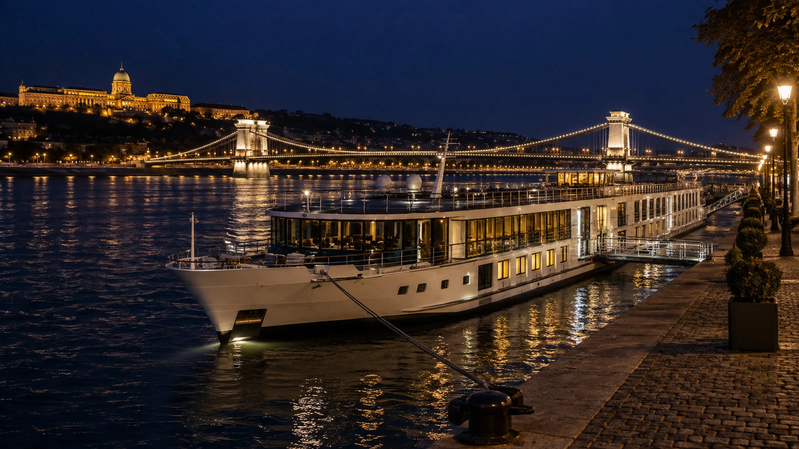 a river cruise ship moored at a different quay near a bridge after dark with no people