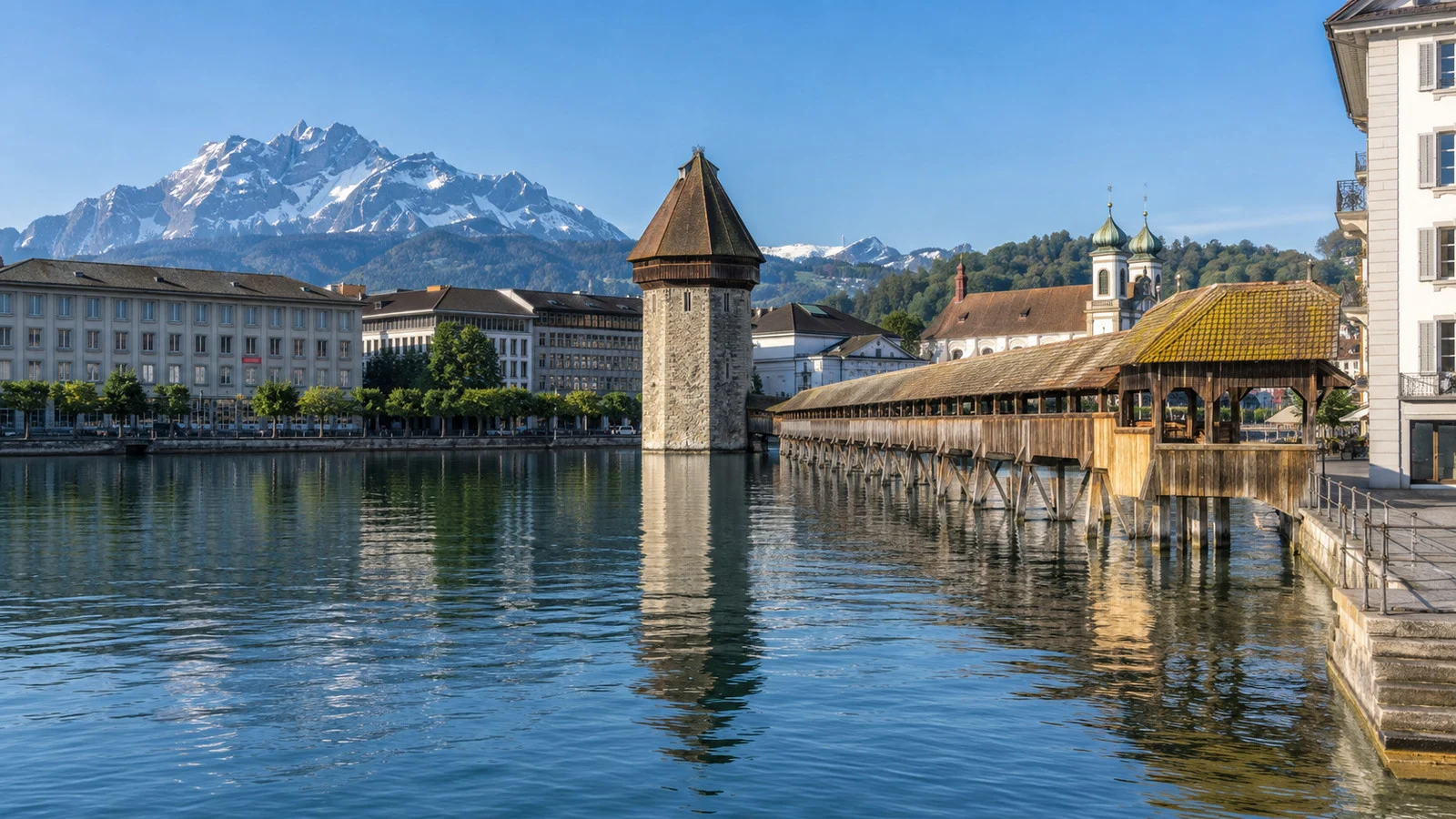 Lucerne lakefront with Chapel Bridge and Alpine mountains in the distance on a clear day